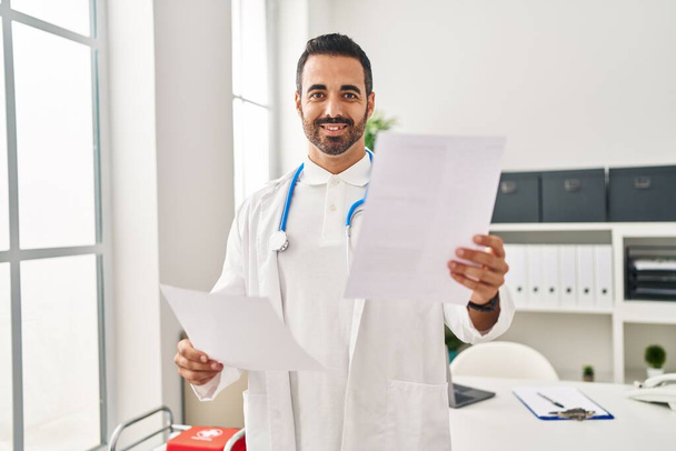 Junger hispanischer Mann in Arztuniform liest Bericht in Klinik - Foto, Bild