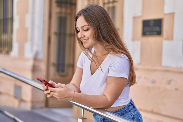Joven mujer rubia sonriendo confiada usando smartphone en la calle - Foto, imagen