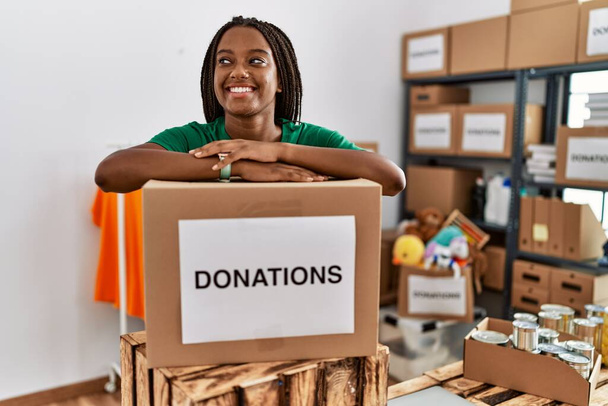 ボランティアの制服を着た若いアフリカ系アメリカ人女性がチャリティーセンターの寄付パッケージにもたれて - 写真・画像