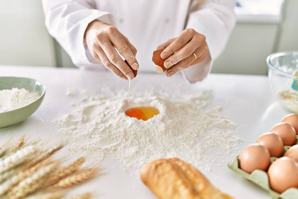 Young woman wearing cook uniform cracking egg on flour at kitchen - Foto, Imagen