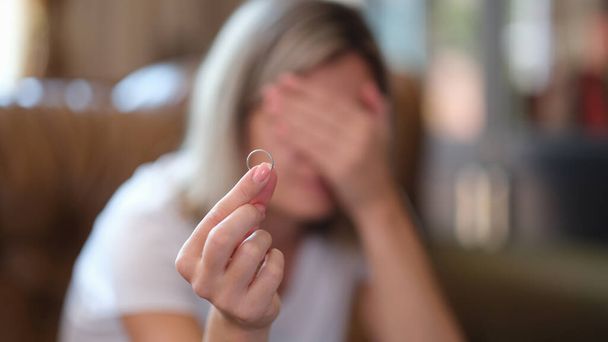 女性は結婚指輪を手に持ち、自宅で泣きます。離婚うつ病とストレス - 写真・画像