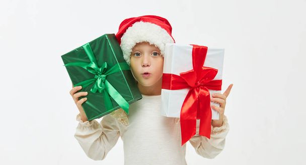 Christmas child. Cute toddler girl in santa claus caps holding colorful gift boxes on white. Wow fanny face. Preparing for New Year's holidays in Italy - Фото, изображение