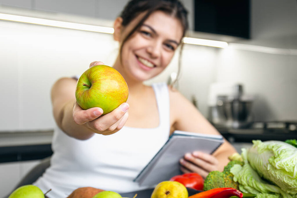 Una joven en la cocina con un cuaderno y verduras, el concepto de cocina, dieta y salud. - Foto, imagen