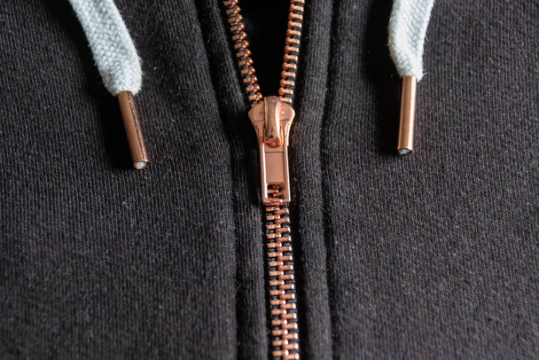 Copper colored fashion zipper in close-up macro view showing black sweatshirt with partial opened metal zipper with black fabric in metallic optic as elegant apparel or stylish fastener solid material - Photo, Image