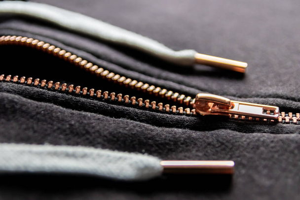Copper colored fashion zipper in close-up macro view showing black sweatshirt with partial opened metal zipper with black fabric in metallic optic as elegant apparel or stylish fastener solid material - Photo, Image