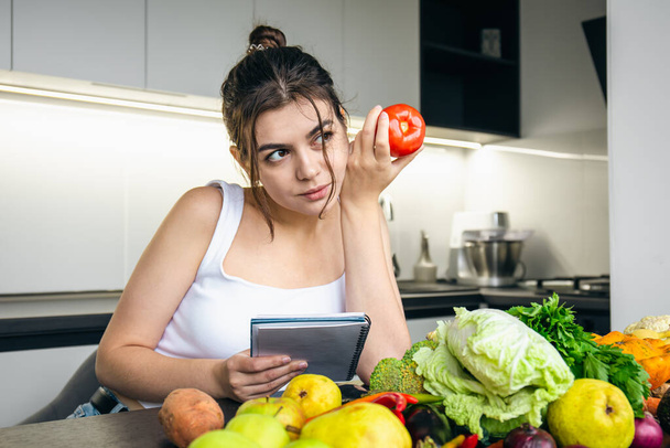 Nuori nainen keittiössä muistikirja käsissään prosessissa ruoanlaitto vihanneksia. - Valokuva, kuva