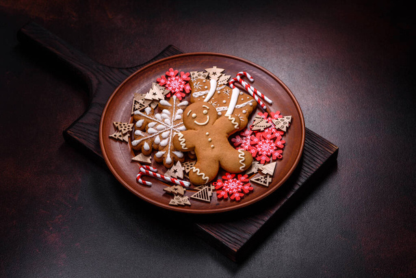 Красивые пряники на коричневой керамической тарелке с украшениями рождественской елки на темном бетонном фоне. Возвращение домой к Рождеству - Фото, изображение