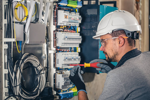 Hombre, un técnico eléctrico trabajando en una centralita con fusibles. Instalación y conexión de material eléctrico
. - Foto, Imagen