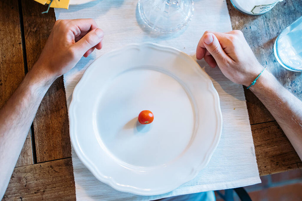 One single cherry tomato on the plate with hands around the plate. Diet concept - Foto, Imagem