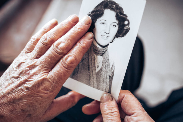 CIRCA 1970: Elderly woman hands holding vintage, black and white photo of the young woman. Passing of time concept - Foto, Bild