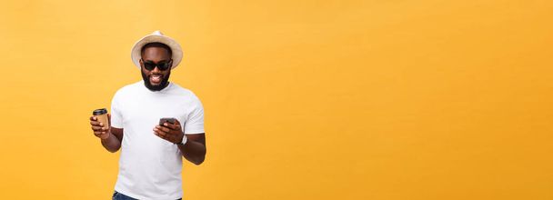 Handsome African American with mobile phone and take away coffee cup. Isolated over yellow gold background - Foto, Imagen