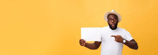 Picture of young smiling african-american man holding white blank board and pointing on it, on yellow background, copy space. - Foto, immagini