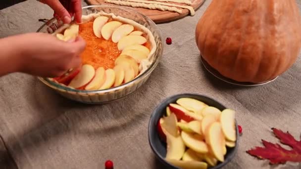 Gros plan sur les mains d'une femme au foyer, étalant des tranches de pomme en cercle sur le dessus de la purée de citrouille dans la pâte roulée dans le plat de cuisson, tout en préparant une délicieuse tarte à la citrouille pour le jour de Thanksgiving - Séquence, vidéo