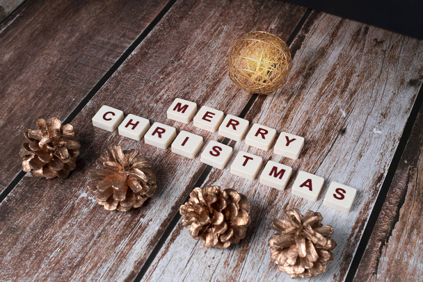 Merry Christmas written with letters of a set and Christmas ornaments with sparkle, on a wooden background. - Фото, изображение