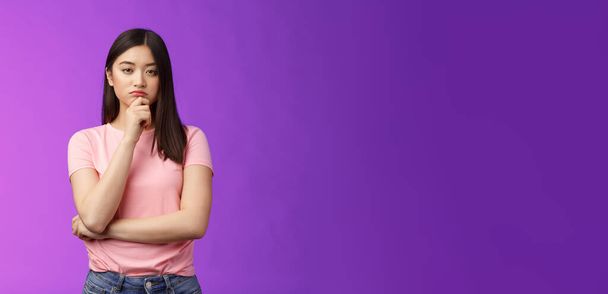 Judgemental serious-looking smart asian girl give expert look, touch chin thoughtful, squinting suspicious uncertain, make decision, choosing product, thinking, pondering plan, purple background. - Photo, Image