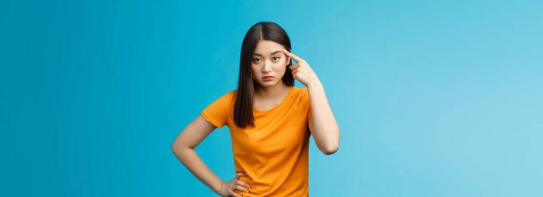 Pissed irritated asian girl look annoyed bend camera roll finger on temple stare camera bothered dismay, asking are you out mind, show person crazy weird, stand blue background. Copy space - Foto, Imagem