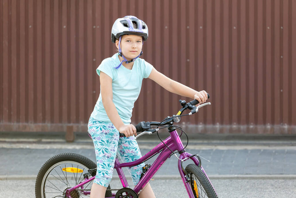 One happy young school age girl biker sitting on a bike smiling Cheerful cyclist kid on a bicycle, children sports leisure and recreation activities outdoors concept, copy space, one person, lifestyle - Photo, Image