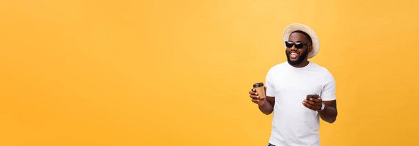 Guapo afroamericano con teléfono móvil y llevar taza de café. Aislado sobre fondo de oro amarillo
 - Foto, Imagen