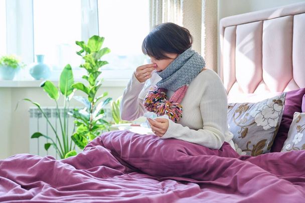 Sick woman holding handkerchief, sneezing, wiping her nose, sitting in bed at home. Health problems, cold flu season, lifestyle, people concept - Foto, imagen