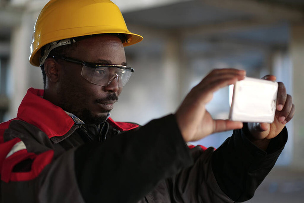 Αφροαμερικάνος εργάτης καταγράφει βίντεο στο smartphone. Διευθυντής των εργασιών στο εργοτάξιο κινηματογράφηση βίντεο - Φωτογραφία, εικόνα