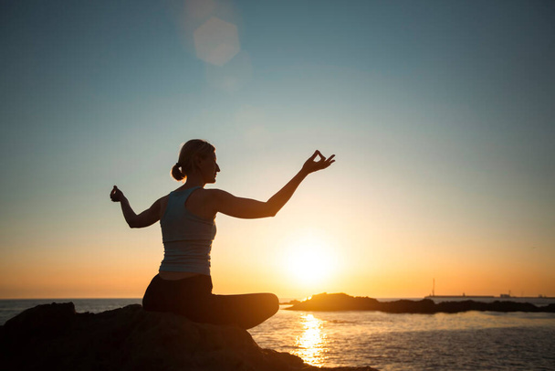 Jooga nainen meditoi lootus asennossa auringonlaskun aikana valtameren rannalla.   - Valokuva, kuva