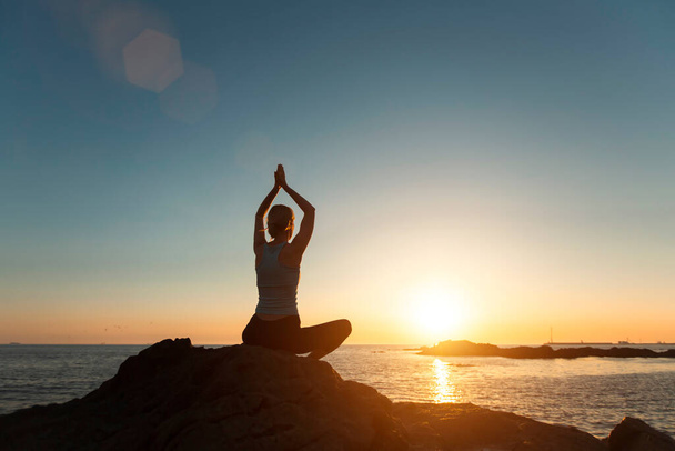 Silhouette einer Yoga-Frau in Lotusposition bei Sonnenuntergang am Meer.   - Foto, Bild