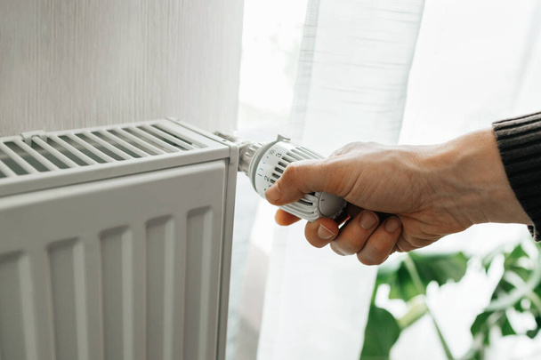 Um homem regula a temperatura no radiador em casa. Aumento dos preços do aquecimento nas famílias. O conceito da crise energética na Europa.  - Foto, Imagem