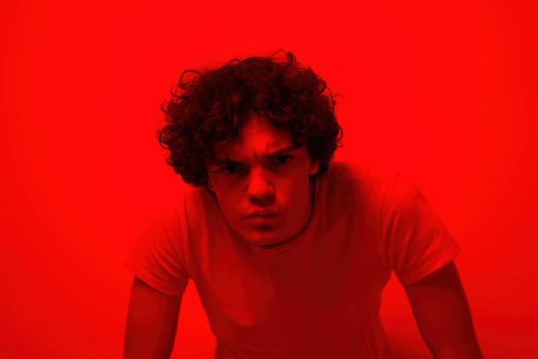 Confident caucasian teenage boy looking at camera. Curly guy of zoomer generation wearing t-shirt. Concept of modern youngster lifestyle. Isolated on red background. Studio shoot. Copy space - Φωτογραφία, εικόνα