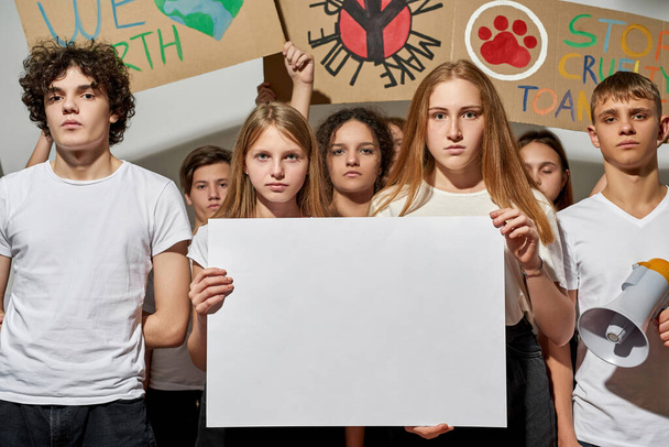 Group of serious caucasian teenagers with peaceful and antiwar placards protesting on democratic rally. Blonde girls holding white empty banner for copy space. Isolated on white background in studio - Fotó, kép