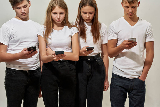 Four caucasian teenage guys and girls of zoomer generation using and browsing smartphones. Idea of gadget addiction. Concept of modern youngster lifestyle. Isolated on white background. Studio shoot - Φωτογραφία, εικόνα