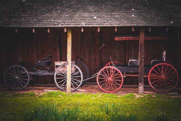 two beautiful vintage horse cart trap vehicle next to a rustic barn stable building - Photo, Image