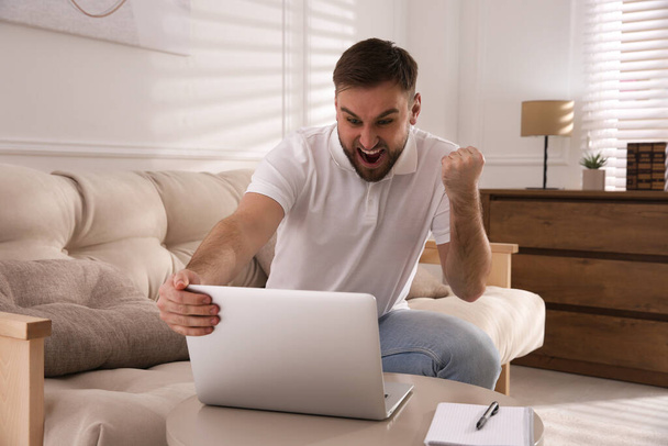 Emotional man participating in online auction using laptop at home - Foto, afbeelding