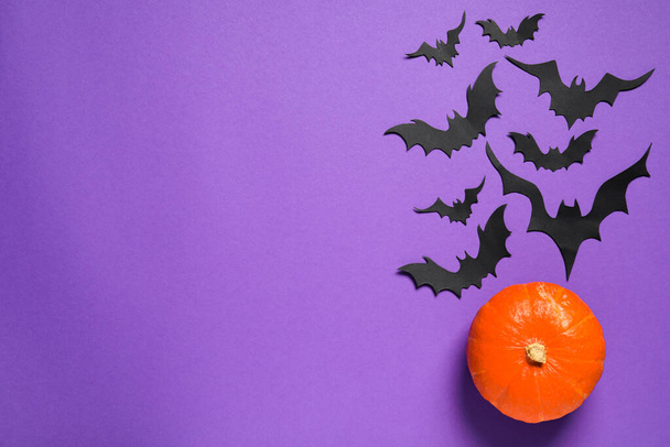 Flat lay composition with pumpkin and paper bats on purple background, space for text. Halloween decor - Fotó, kép