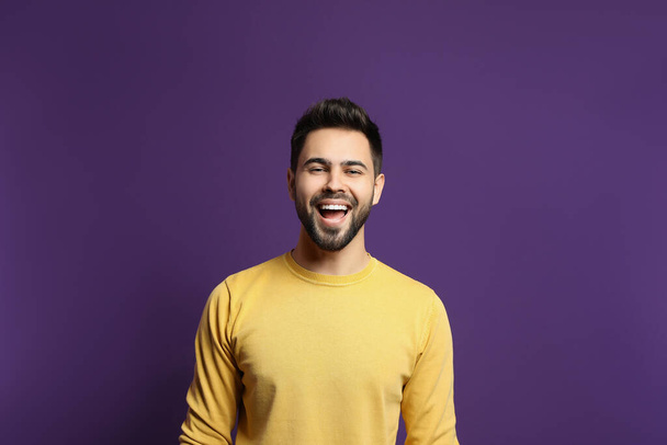 Young man laughing on purple background. Funny joke - 写真・画像