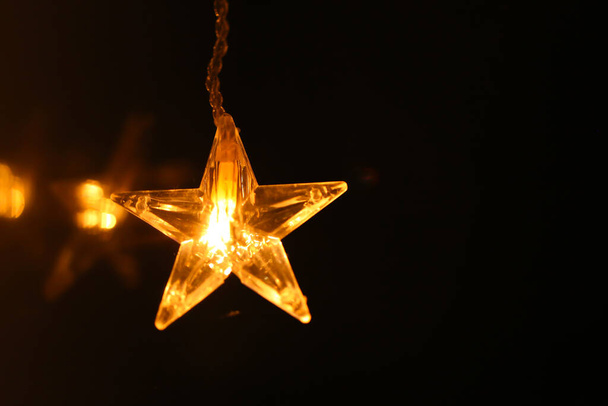 Christmas wallpaper.Star burning on a black background.Festive glowing garlands on a dark background.Christmas and New Year festive background. - Φωτογραφία, εικόνα