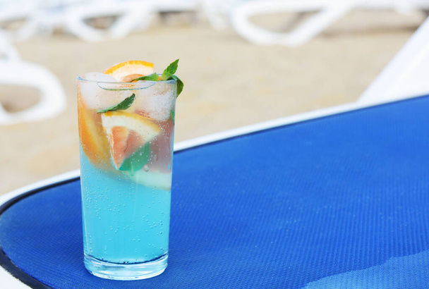 Un vaso de bebida refrescante con pomelo y menta en una tumbona azul en la playa, espacio para el texto - Foto, Imagen