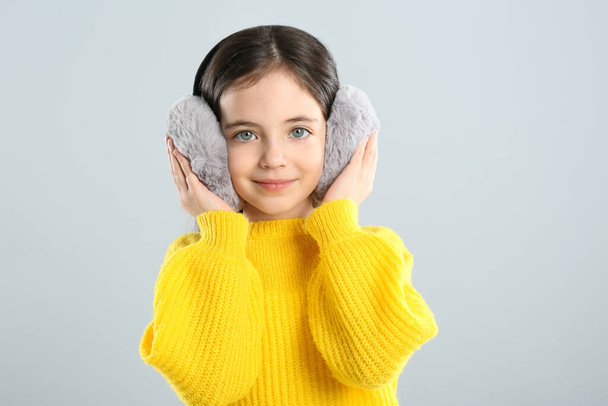 Cute girl wearing stylish earmuffs on grey background - Фото, изображение