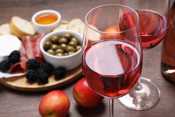Delicious rose wine and snacks on wooden table, closeup - Fotó, kép