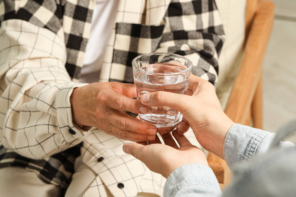 Caretaker giving glass of water to elderly woman indoors, closeup - Fotografie, Obrázek