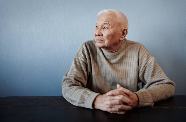 Pensieve en bedachtzame oudere man zittend aan tafel - Foto, afbeelding