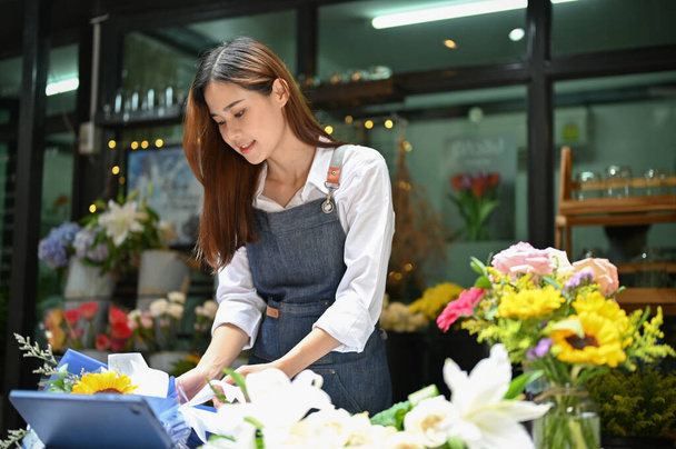Wspaniałe millenium Azji kobieta kwiaciarnia lub kwiaciarnia pracownik w fartuchu organizując bukiet kwiatów dla klienta. - Zdjęcie, obraz