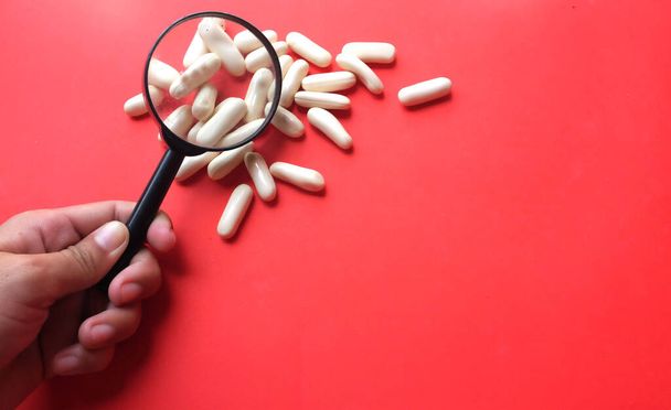  pharmaceutical medicine pills, tablets, capsules under the magnifying glass isolate on a  red background. Minimal modern pharmacy or health care concept. Flat lay - 写真・画像