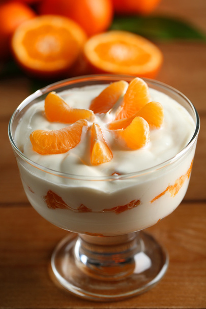 Tasty milk dessert with fresh tangerine pieces in glass bowl, on wooden background - Photo, image