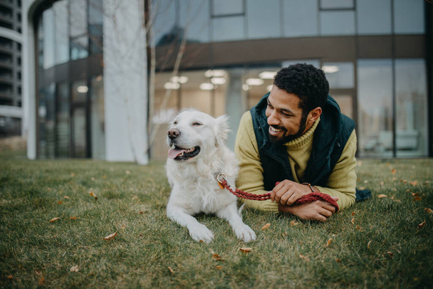 Glücklicher junger Mann, der sich an einem kalten Herbsttag mit seinem Hund im Stadtpark ausruht. - Foto, Bild