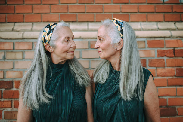 Portrait of senior women, twins,in same clothes standing back to back, outdoor in a city. - Fotoğraf, Görsel