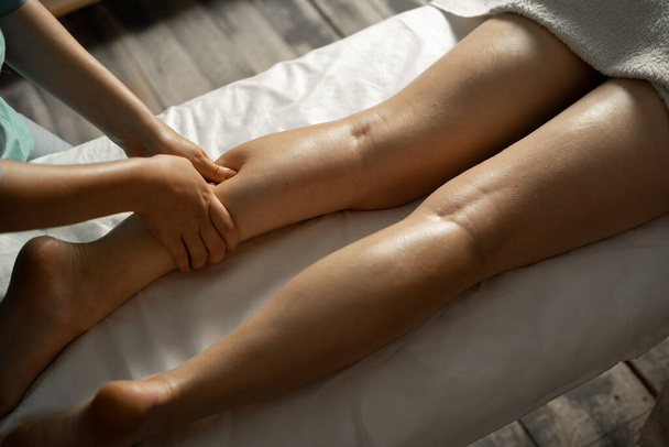 Массер робить масаж ніг у спа-салоні, зблизька. Масаж-терапевт працює з пацієнтом, масажуючи його телят.. - Фото, зображення
