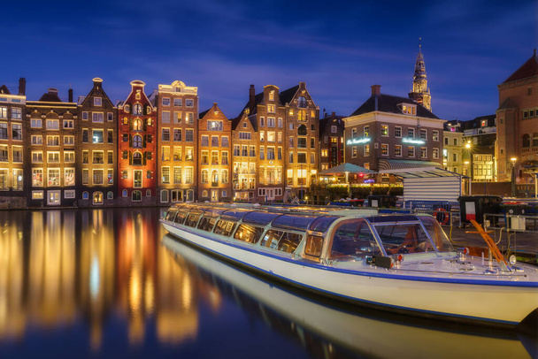 Damrak, Amsterdam, Netherlands. View of houses and boats during sunset. The famous Dutch canals and boats. A cityscape in the evening. Travel photography. - Foto, Imagem