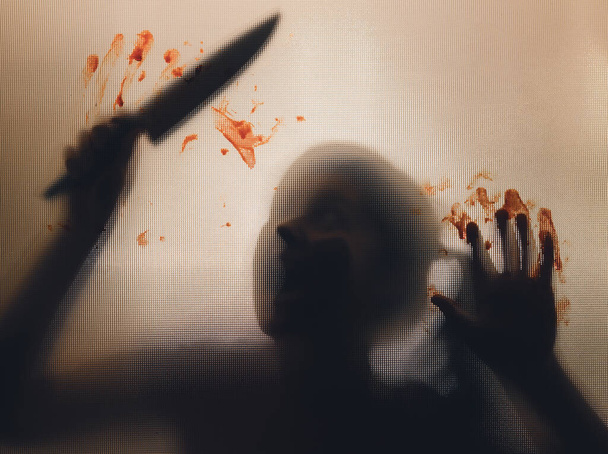 Horror, halloween background - Shadowy figure behind glass holding a knife with blood - Foto, Imagem