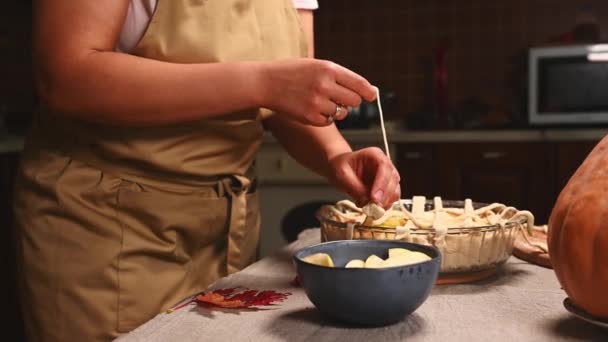Κοντινό πλάνο μιας νοικοκυράς με μπεζ ποδιά σεφ, διακοσμώντας την κλασική αμερικάνικη σπιτική εορταστική πίτα με ένα τραγανό πλέγμα ζαχαροπλαστικής. Ημέρα των Ευχαριστιών. Φτιάχνοντας νόστιμη μηλόπιτα κολοκύθας με κρούστα. - Πλάνα, βίντεο