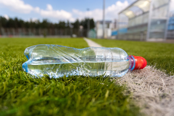пластикова пляшка води лежить на трав'яному футбольному полі
 - Фото, зображення